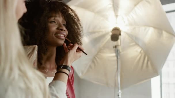 Backstage of the Photo Shoot : Make-up Artist Applies lipstick Makeup on Beautiful Black Girl. Modèle professionnel Se préparer pour Photoshoot pour un magazine de mode dans un studio. Tir à l'arc — Video