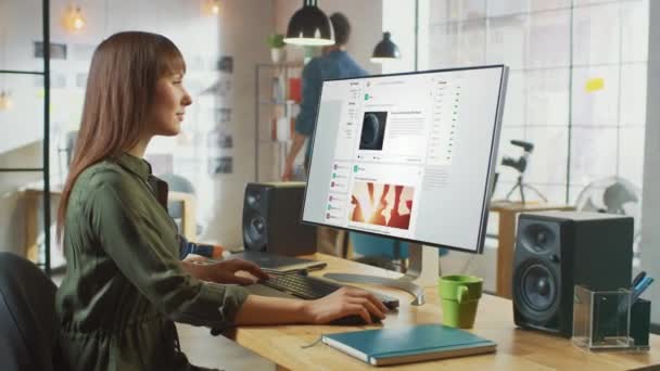 Vackra Brunett Kvinnliga Rullar genom sociala medier webbplats på hennes persondator med stor skärm. Hon jobbar på ett coolt kontor. Andra manliga kreativa Colleague promenader i bakgrunden. — Stockvideo