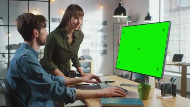 La directora de arte femenina consulta a su colega diseñadora, trabajan en una computadora personal con pantalla verde Mock Up Display. Trabajan en un Cool Office Loft. Se ven muy creativos y frescos. — Vídeo de stock