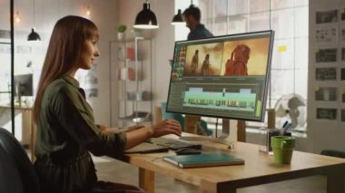 Güzel Esmer Kadın Video Düzenleyicisi Büyük Ekranla Kişisel Bilgisayarında Görüntü Çalışıyor. Havalı bir ofisin çatı katında çalışıyor. Diğer Erkek Yaratıcı Meslektaşlar Arkaplanda Yürüyor.