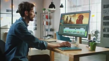 Sakallı Erkek Video Editörü ve Büyük Ekran ile Kişisel Bilgisayarında Çalışır. Havalı bir ofisin çatı katında çalışıyor. Diğer Yaratıcı Kadın Meslektaşlar Arkaplanda Yürüyor.