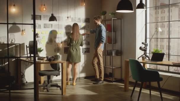 Junge kreative Männer und Frauen organisieren ein Stimmungsbrett an einer Wand ihres coolen Büro-Lofts. Bilder repräsentieren Future Motion Video. Kollegen arbeiten und diskutieren an dem Projekt. Sonniger Tag. — Stockvideo