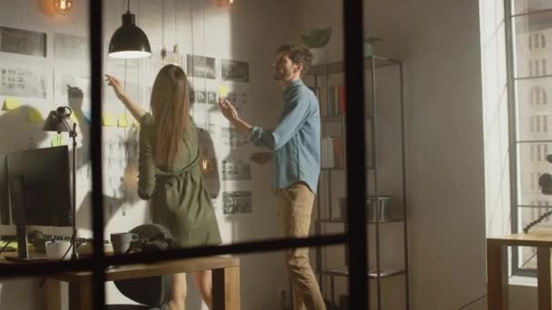 Unga kreativa män och kvinnor organiserar en Storyboard på en vägg av deras Cool Office Loft. Bilder Representera Framtida Rörelse Video. Kollegerna arbetar och diskuterar projektet. Solig dag. — Stockvideo