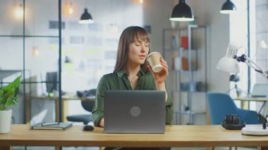 Havalı Yaratıcı Ajans 'ın çatı katında dizüstü bilgisayarda çalışan genç, güzel esmer kadın. Paket kahve içiyormuş. Kamera yaklaşır ve o gülümser ve güler..