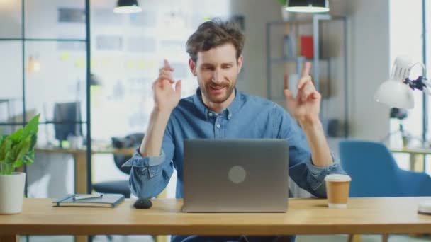 Joven hombre guapo trabaja en una computadora portátil en Cool Creative Agency en Loft Office. Lleva una camisa vaquera. Él es feliz, sonriendo, bailando y se divierte. — Vídeo de stock