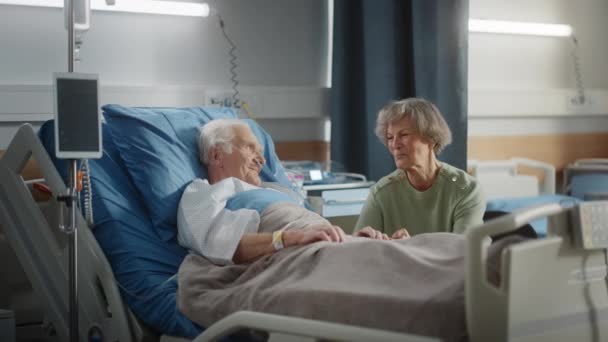 Hospital Ward Old Husband en la cama habla con su esposa visitando — Vídeos de Stock