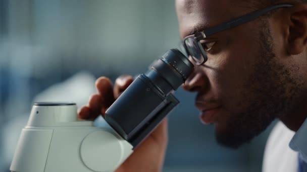 Macro metraggio nero maschio scienziato utilizzando il microscopio in laboratorio — Video Stock