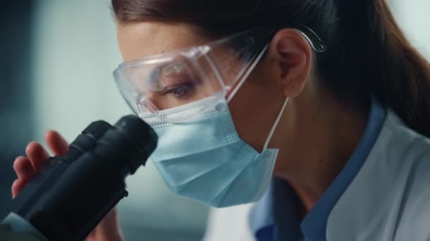 研究室で顕微鏡を使って顔マスクの女性科学者を閉じる — ストック動画