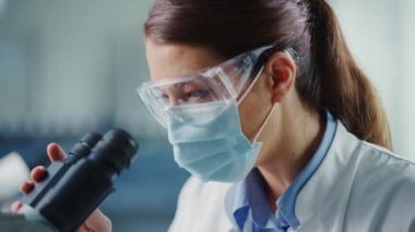 Laboratuvarda Kadın Maskeli Bilimadamını Mikroskop kullanarak Kapat