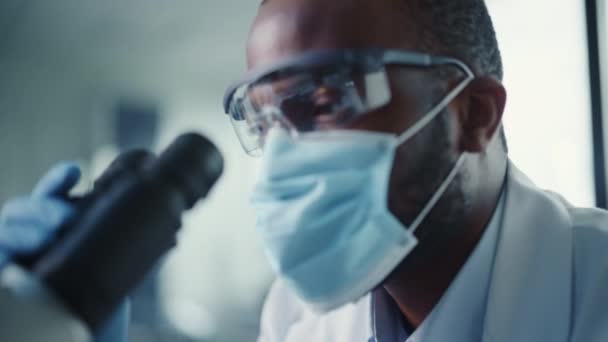 Close Up Black Male Scientist in Face Mask Using Microscope in Laboratory — Stock video