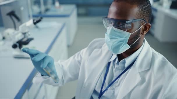 Närbild svart man forskare i ansiktsmask Tittar på prov i Petri Dish i laboratoriet — Stockvideo