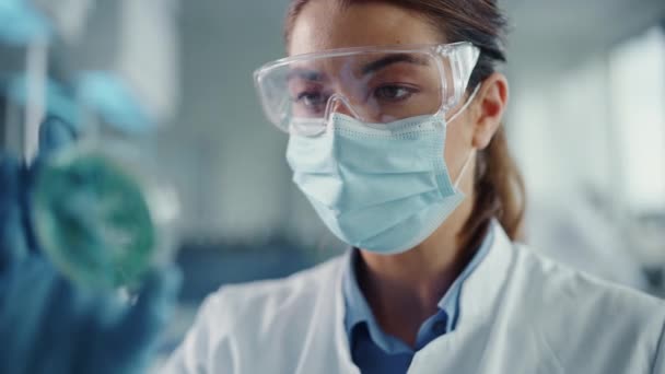 De cerca Científica femenina en la máscara de cara mirando la muestra en Petri Plato en el laboratorio — Vídeos de Stock