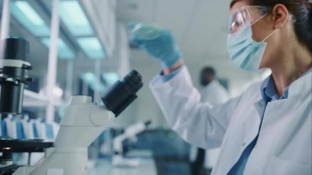 De cerca Científica femenina en la máscara de cara mirando la muestra en Petri Plato en el laboratorio — Vídeos de Stock