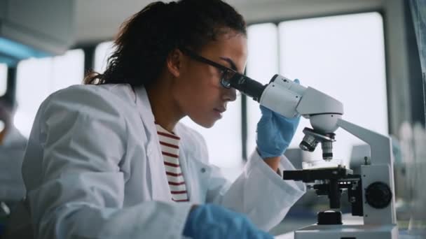 Científica joven en laboratorio Mirando bajo microscopio — Vídeo de stock