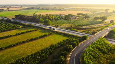 Aerial Drone Shot: Long Haul Semi Truck Driving on the Busy Highway in the Rural Region of Italy. Beautiful Scenery of Nature and Human Logistics Progress clipart