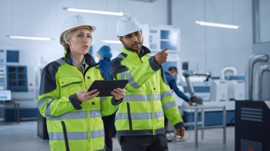 Güvenlik Yelekleri ve Sert Şapkalar Baş Mühendisi ve Proje Yöneticisi Modern Fabrikada Yürüyor, Konuşuyor, Üretimi İyimserleştiriyor. Endüstriyel Tesis: Profesyoneller Makineleri Kullanıyor.