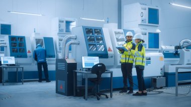 Güvenlik Yelekleri ve Sert Şapkalar Giyen Baş Mühendis ve Proje Yöneticisi, Fabrikada Dijital Tablet Kontrolörü Kullan, Üretim Hattı Verimliliğini Artırmak İçin CNC Makine Programlama Makinesini İyimser Et 