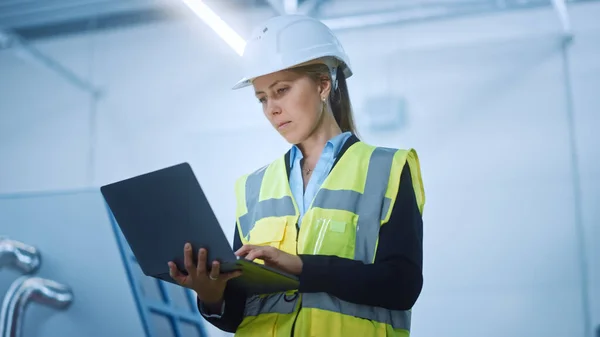 ハイテク工場:安全ジャケットとハード帽子の保持を身に着けている自信とプロの女性エンジニアとラップトップコンピュータで働く。近代的な明るい産業施設。ローアングルショット — ストック写真