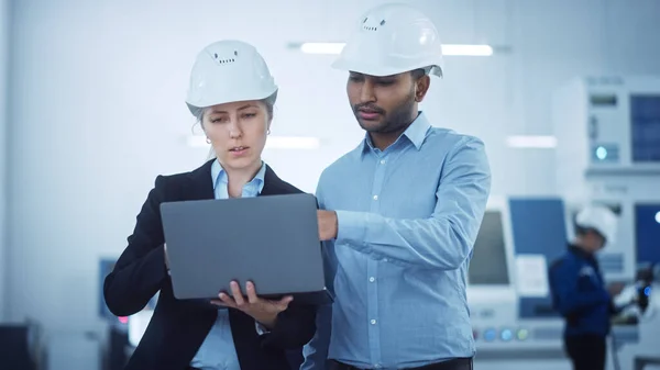 Γυναίκα Chief Engineer και Male Project Managers Standing in the Middle of Modern Factory, Χρήση Laptop Computer, Βελτιστοποίηση Γραμμής Παραγωγής Σχεδίου. Επαγγελματίες άνθρωποι εργάζονται σε βιομηχανικά CNC μηχανήματα — Φωτογραφία Αρχείου