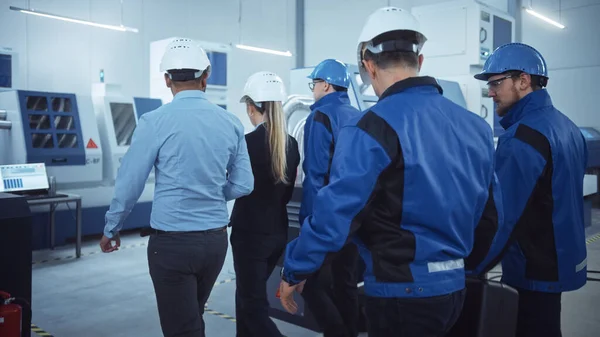 女首席项目管理员、工程师小组、工人、安全、戴硬帽的控制检查员穿过工厂。配备现代数控机床.侧视图 — 图库照片