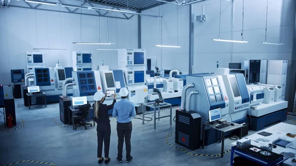 Fábrica moderna: Dos ingenieros utilizan la computadora digital de la tableta con la realidad aumentada que visualiza el mapeo de la sala de taller, el diseño del piso. Instalación con maquinaria CNC de alta tecnología y brazo robot. Ángulo alto — Foto de Stock