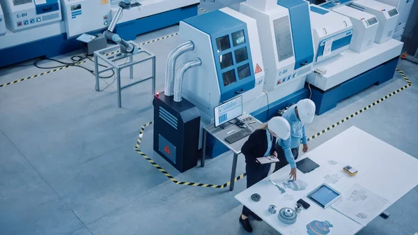 Przemysł Cztery fabryki: Kobieta wykonawcza i główny inżynier inspekcji obiektu Warsztaty, Spójrz na ramię robota pracy na linii montażowej, Analizuj plany wysokiej klasy maszyn i urządzeń CNC. Kąt wysoki — Zdjęcie stockowe