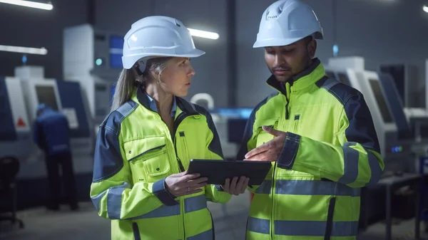 总工程师兼项目经理穿着安全背心和硬帽，在现代工厂使用数字制表机，说话，优化生产线。带有数控机床的工业设施 — 图库照片