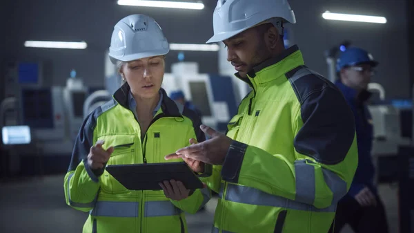 Engenheiro chefe e gerente de projeto vestindo coletes de segurança e chapéus duros, Use Digital Tablet Computer na fábrica moderna, Falando, Otimizando a linha de produção. Instalação industrial com máquinas CNC — Fotografia de Stock