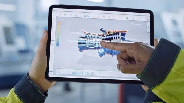 Fábrica de Industria 4.0: Ingeniero Jefe y Supervisor de Proyectos en Chalecos de Seguridad y Sombreros Duros, Conversación, Uso de Tablet Digital, Pantalla Muestra el Concepto 3D del Nuevo Motor a reacción. Taller con maquinaria. — Foto de Stock