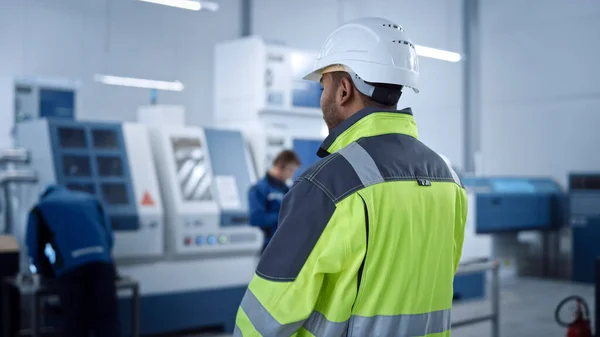 Industrial 4 Factory: Modern Worker Wearing Safety Jacket and Hard Hat, Walks Through Contemporary Industrial Workshop which Professionals are Working and Programming CNC Machinery. — 스톡 사진