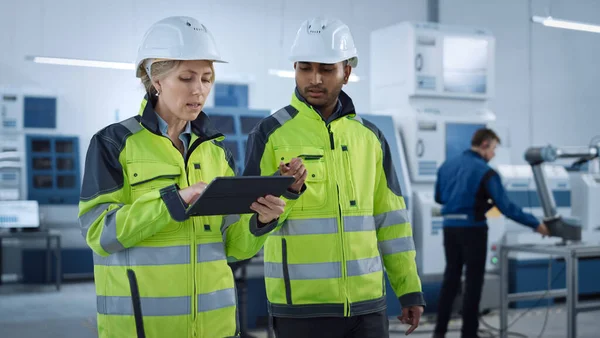 Hoofdingenieur en projectleider in veiligheidsvesten en harde hoeden lopen door de moderne fabriek, praten, optimaliseren van de productie. Industriële faciliteit: Professionals gebruiken machines. — Stockfoto