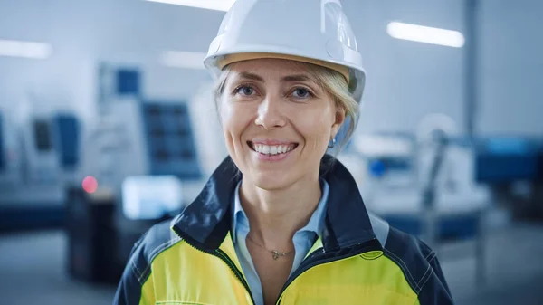《安全背心和硬礼帽》相机女工程师美丽微笑的肖像。在现代制造业工厂工作的职业女性。数控机床机械臂装置 — 图库照片