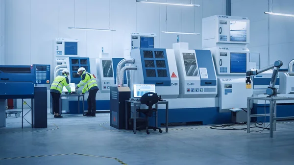 수석 엔지니어 및 프로젝트 관리자 Wearing Safety Vests and Hard Hats Work on Computer, Talk, Optimize Production Line. 2013 년 6 월 1 일에 확인 함 . on foreground: industry 4.0 Modern Factory with CNC Machinery and robot arm — 스톡 사진