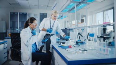 Modern Tıbbi Araştırma Laboratuvarı: Dijital Tablet kullanan iki kadın bilim adamı biyokimyasal örnekleri analiz ediyor. Tıp Bilimsel Laboratuvarı, Mikrobiyoloji Geliştirme. Gelişmiş Ekipman