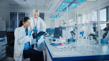 Modern Tıbbi Araştırma Laboratuvarı: Dijital Tablet kullanan iki kadın bilim adamı biyokimyasal örnekleri analiz ediyor. Tıp Bilimsel Laboratuvarı, Mikrobiyoloji Geliştirme. Gelişmiş Ekipman