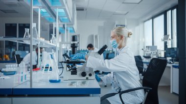 Modern Tıbbi Araştırma Laboratuvarı: Yüz maskesi takan kadın bilim adamının portresi Mikroskop kullanıyor, Test Örnekleri Analiz ediliyor. Gelişmiş Tıp, Mikrobiyoloji Geliştirme Laboratuvarı