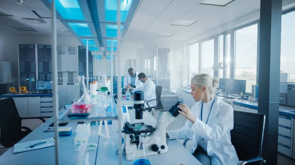 Modern Medical Research Laboratory: Team of Scientists Working with Pipette, Analysing Microbiological Sample, Talking. Advanced Scientific Lab for Drugs, Microbiology Development. High-Tech Equipment