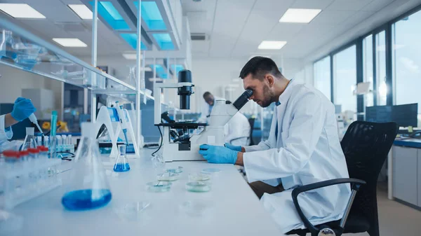 Modern Medical Research Laboratory: Male Scientist Working with Microscope, Analysing Biochemical Samples (dalam bahasa Inggris). Advanced Scientific Lab for Medicine, Microbiology Development. — Stok Foto