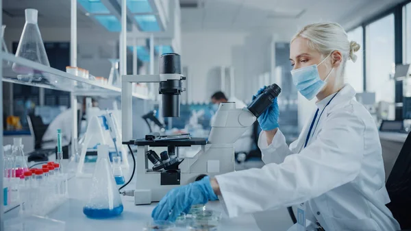 Modern Tıbbi Araştırma Laboratuvarı: Yüz maskesi takan kadın bilim adamının portresi Mikroskop kullanıyor, Test Örnekleri Analiz ediliyor. Gelişmiş Tıp, Mikrobiyoloji Geliştirme Laboratuvarı