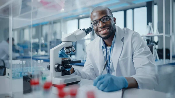 Modern Medical Research Laboratory: Portrait of Male Scientist Using Microscope, Charmingly Smiling on Camera. Advanced Scientific Lab for Medicine, Biotechnology, Microbiology Development — Stock Photo, Image