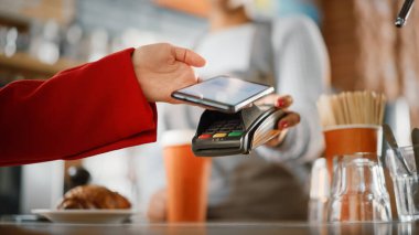 Bir kafede kahveye ödeme yapmak için kullanılan NFC Ödeme Teknolojisi ile akıllı telefonu tutan bir kadının elini kapatın. Müşteri, Latte 'yi Kredi Kartı Terminali aracılığıyla ödemek için Cep Telefonu Kullanıyor.