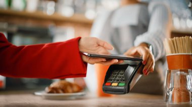 Bir kafede kahveye ödeme yapmak için kullanılan NFC Ödeme Teknolojisi ile akıllı telefonu tutan bir kadının elini kapatın. Müşteri, Latte 'yi Kredi Kartı Terminali aracılığıyla ödemek için Cep Telefonu Kullanıyor.