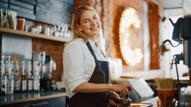 Sarışın, genç, beyaz bir barista bir kafede bir fincan taze kahve yapıyor. Mutlu ve Gülümseyen Bar çalışanı pozu. Rahat bir kafede çalışırken çekilmiş pozlar..