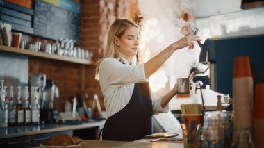 Sarışın, genç, beyaz bir barista bir kafede bir fincan taze kahve yapıyor. Mutlu ve Gülümseyen Bar çalışanı pozu. Rahat bir kafede çalışırken çekilmiş pozlar..