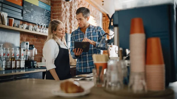 Two Diverse Entrepreneurs Have a Team Meeting in Their Stylish Coffee Shop. Barista and Cafe Owner Discuss Work Schedule and Menu on Tablet Computer. Young Female and Male Restaurant Employees.