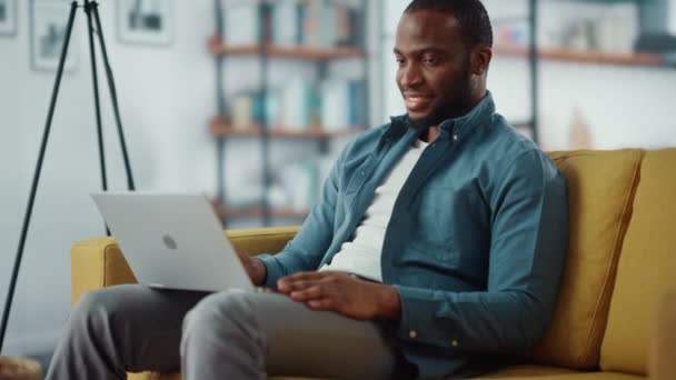 Hombre con ordenador portátil sentado en la sala de estar — Vídeos de Stock