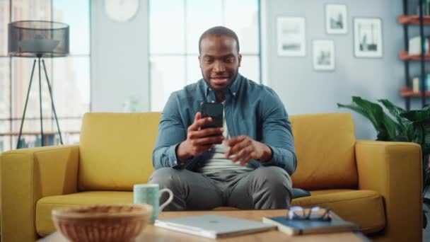 Мужчина со смартфоном сидит в гостиной — стоковое видео