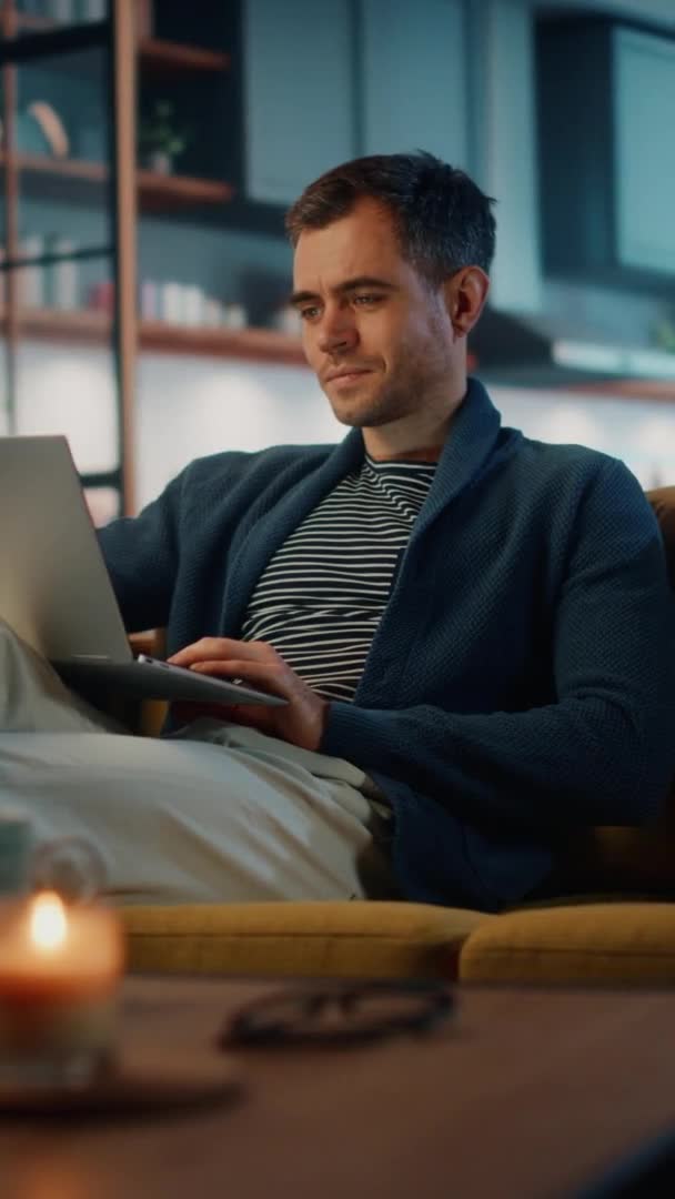 Tiro vertical macho con ordenador portátil sentado en la sala de estar — Vídeos de Stock