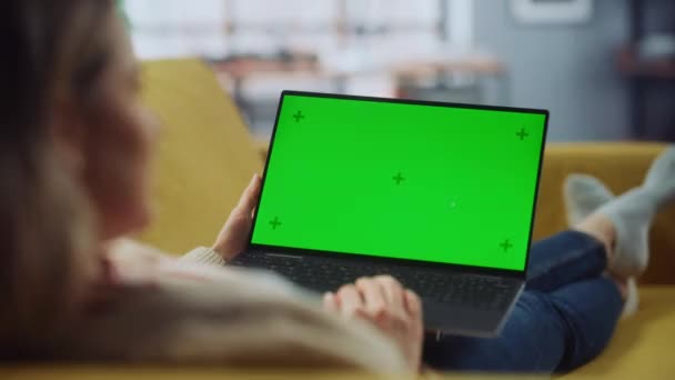 Mujer usando ordenador portátil con pantalla verde en la sala de estar — Vídeos de Stock
