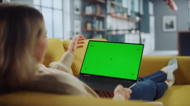 Vrouw met behulp van laptop met groen scherm in de woonkamer — Stockvideo